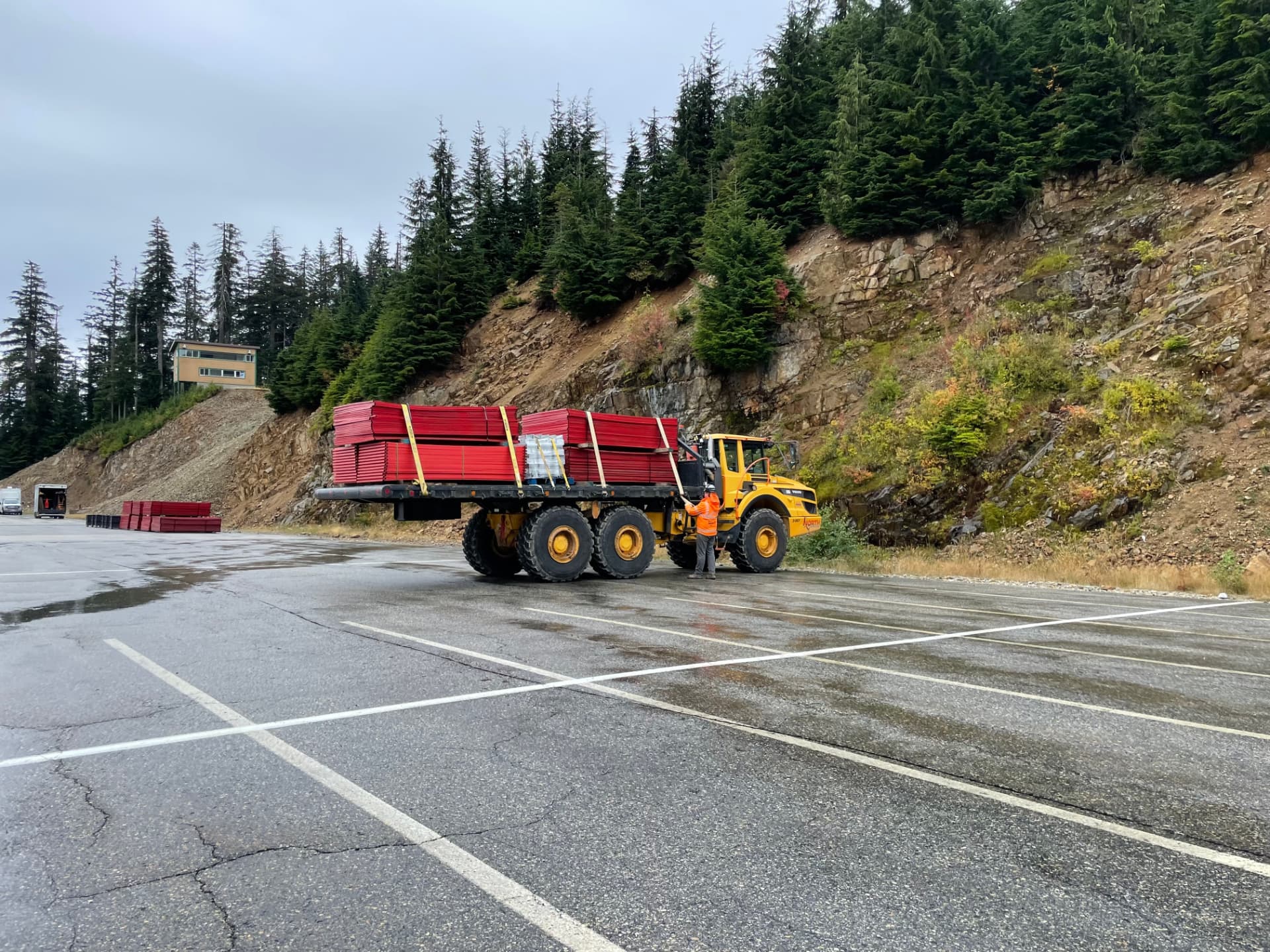 Loader carrying bundled red Clearline temporary fence panels at a forested mountain site